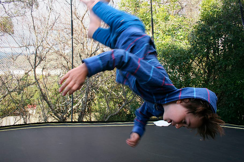 niño haciendo piruetas en un trampolin grande